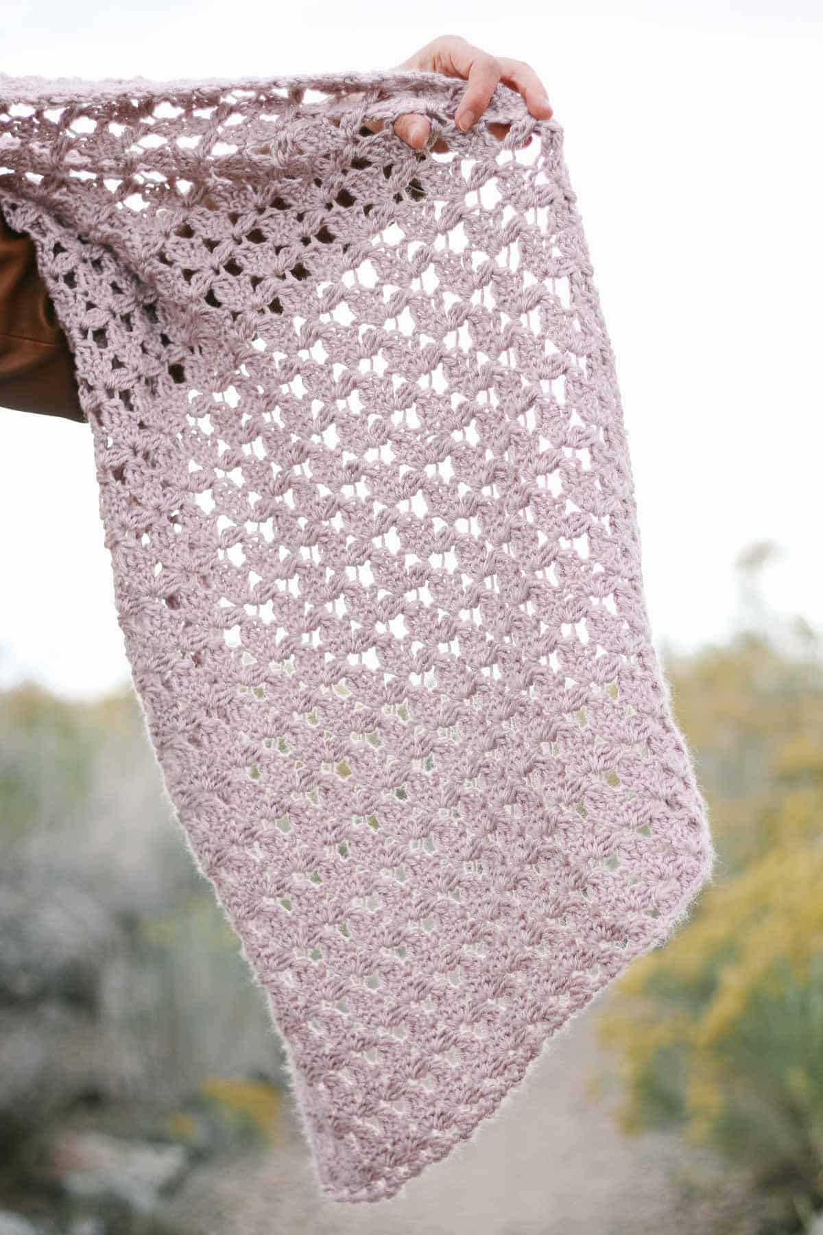 A woman's hand holding a crochet lace scarf.