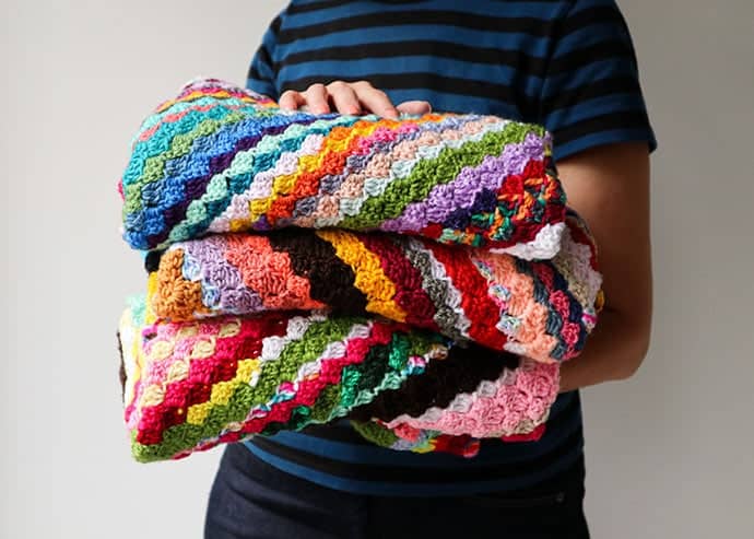 A woman holding three scrappy corner to corner blankets.