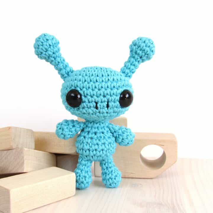 blue alien amigurumi doll with wooden blocks at the back.
