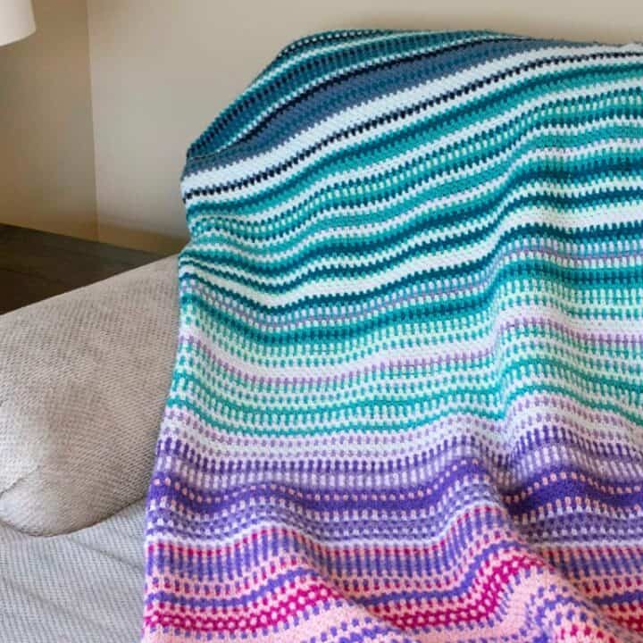 A temperature blanket draped on a white chair.