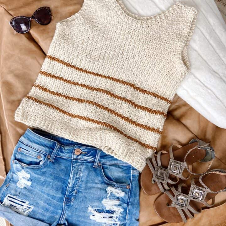 A striped crochet tank top with ripped denim shorts, and sandals on top of a bed.