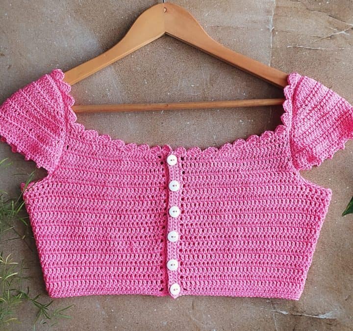 A pink crochet crop top with sleeves and buttons on a hanger.