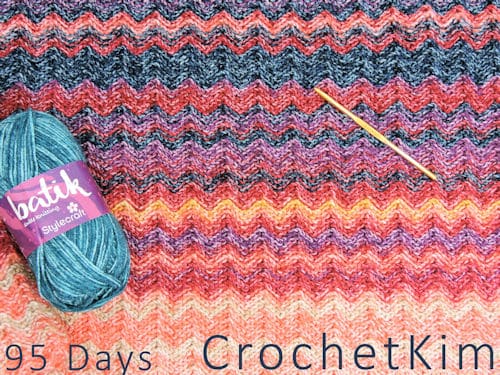 A crochet temperature blanket with a hook and blue yarn skein.