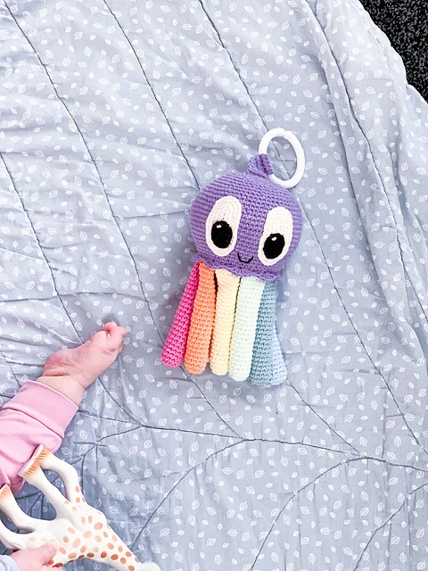 A crochet octopus toy with a handle on a blanket with a baby and a giraffe toy.