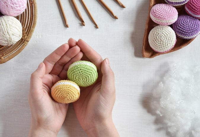 Hands holding crochet oval shapes that look like macaroons. 