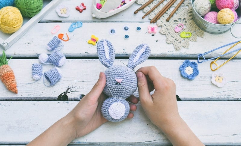 A woman's hands working on a crochet bunny toy.