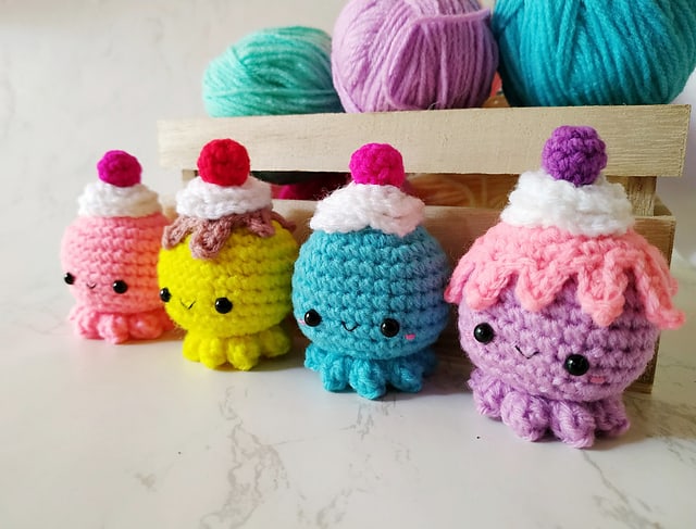 Four different colored cupcake octopuses with a basket full of yarns.
