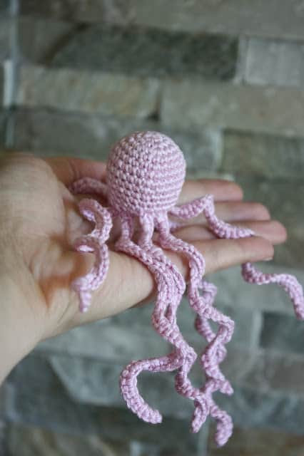 A hand holding out a pink octopus with long tentacles.