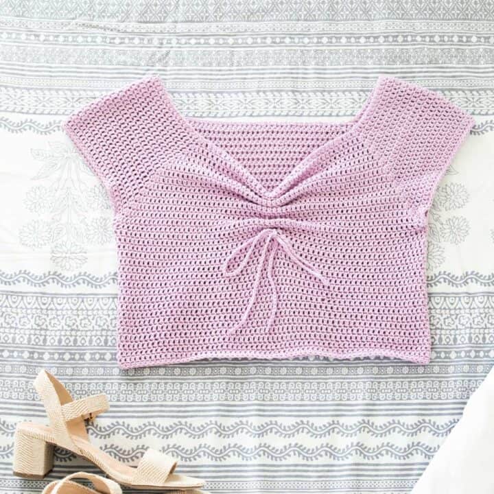 A crochet top with a sweetheart neckline and bow tie detail with a pair of heels on top of a table.
