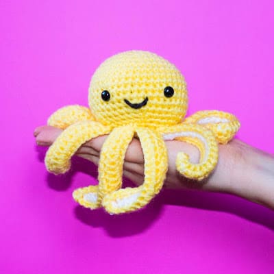 A hand holding a yellow octopus amigurumi.