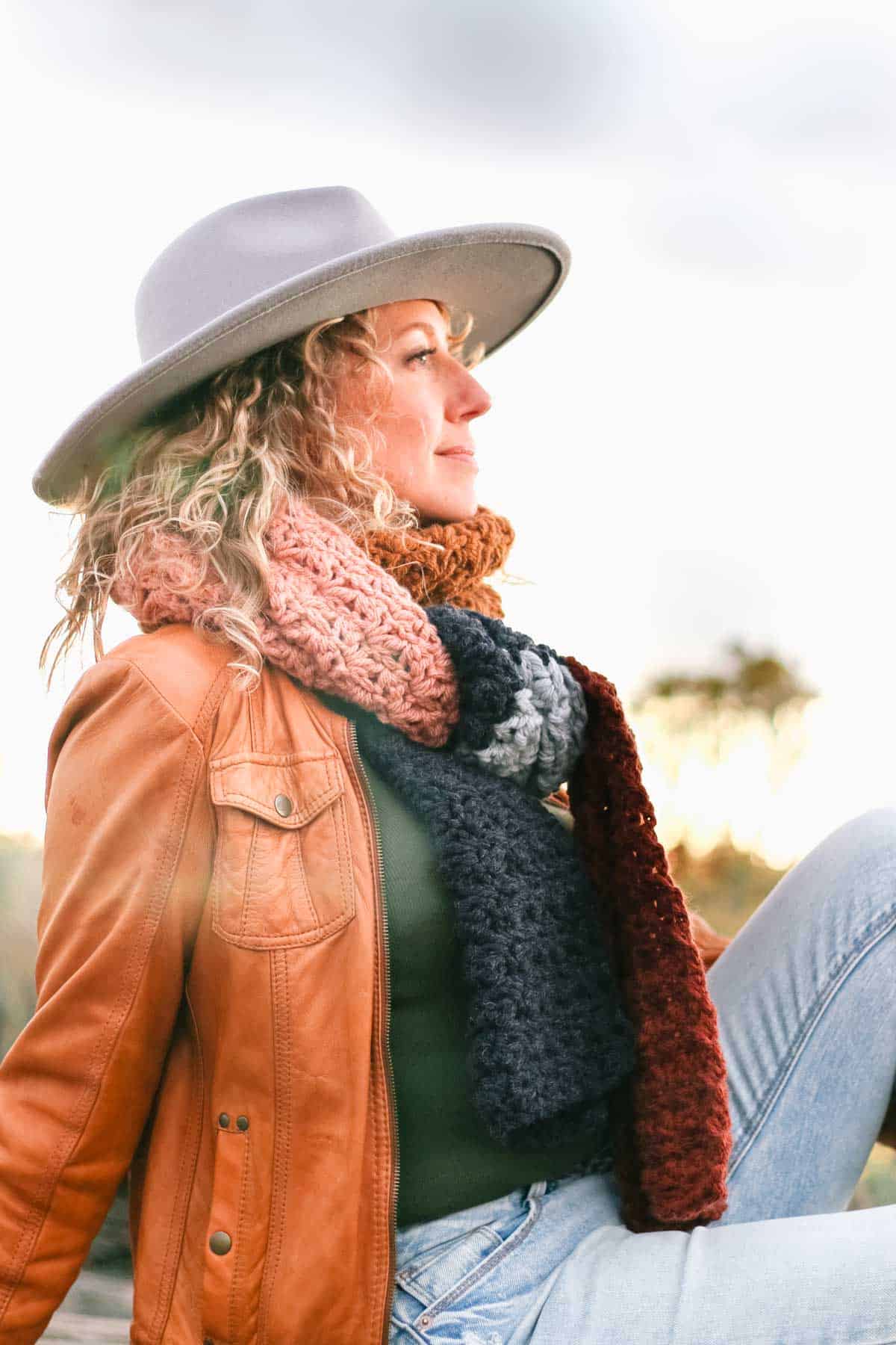 A woman sitting on the grass wearing a fedora hat and an easy, chunky crochet scarf.