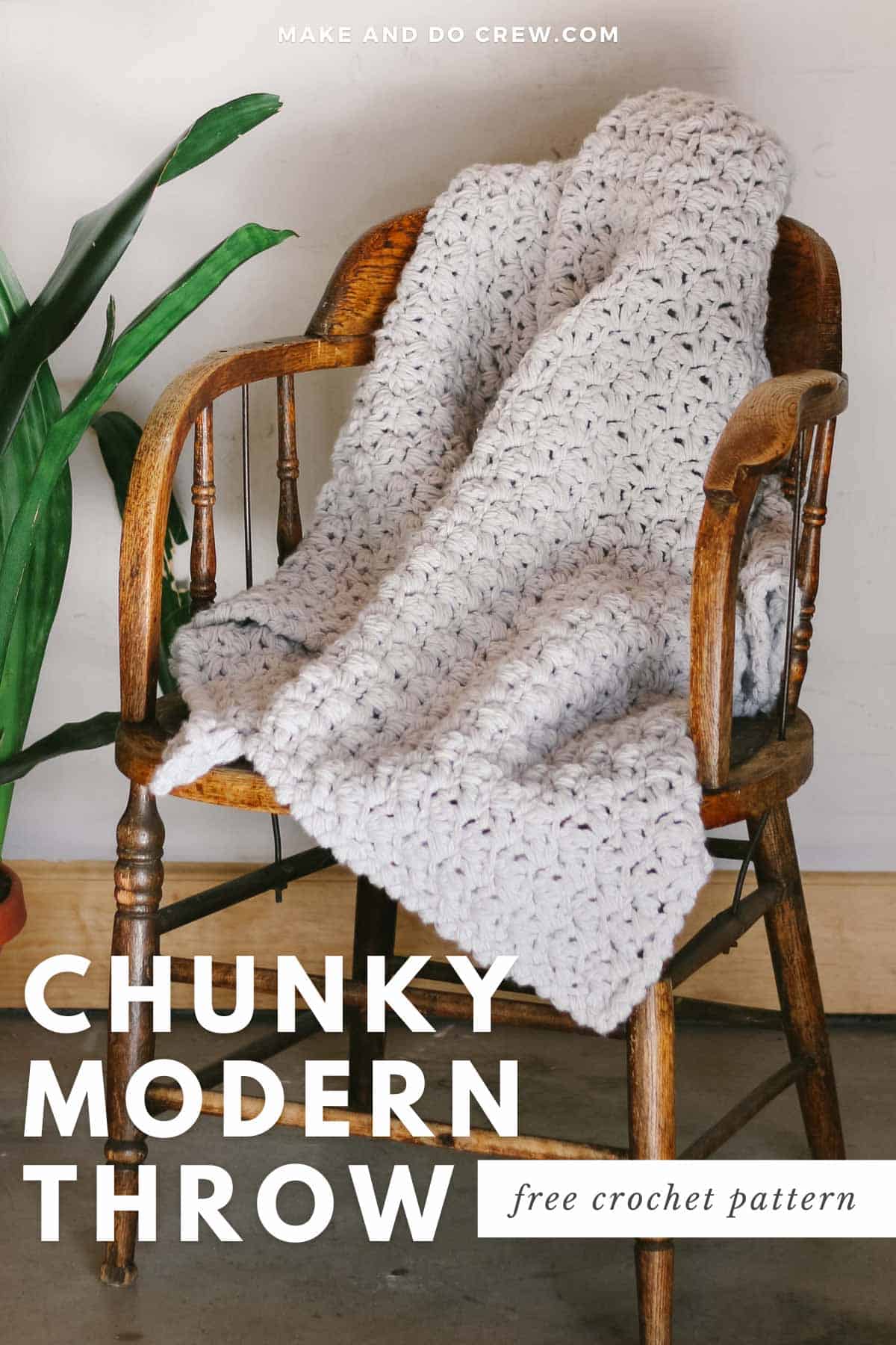 A chunky crochet throw blanket draped on a wooden chair.