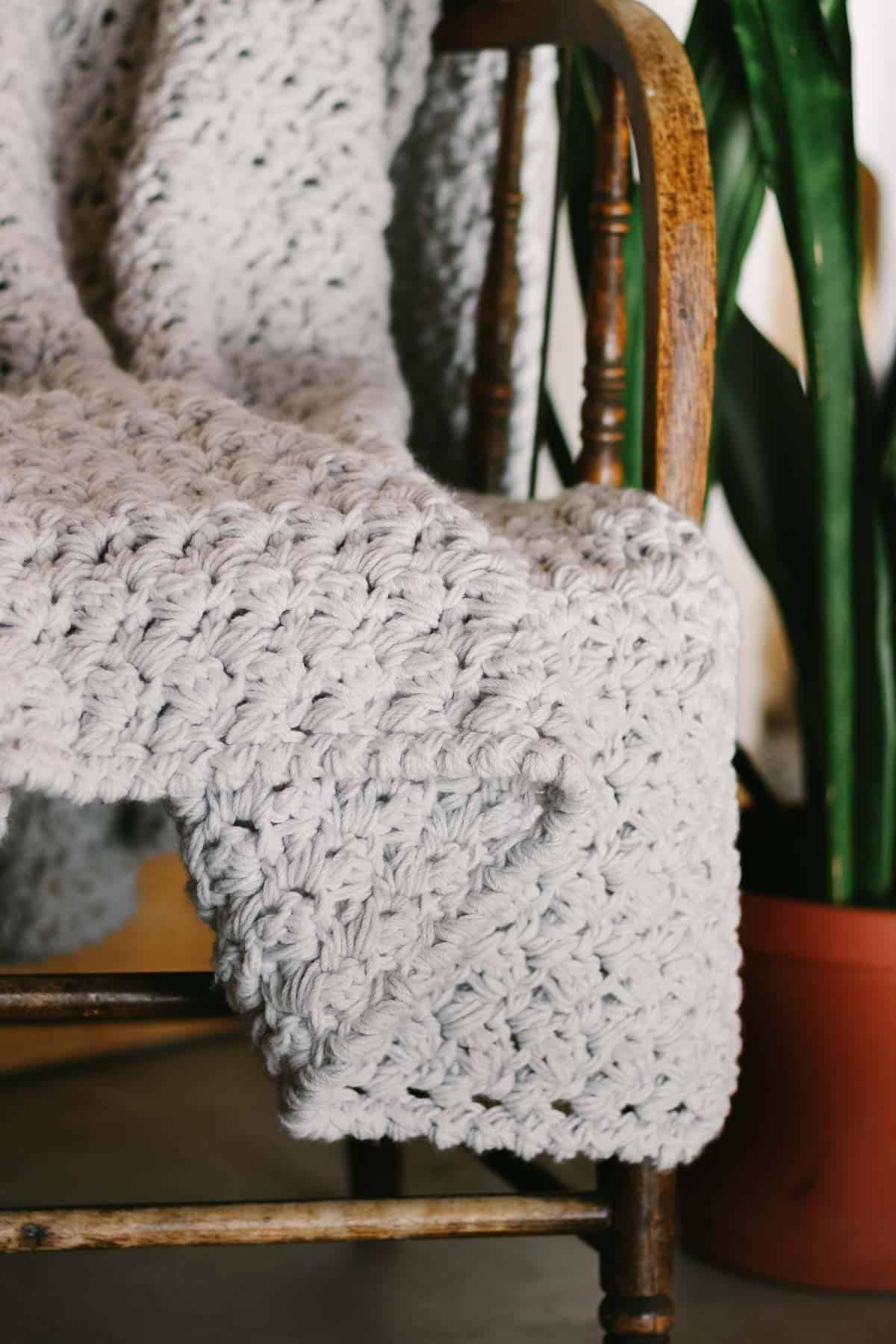 light gray-colored chunky crochet throw blanket draped on a wooden chair.