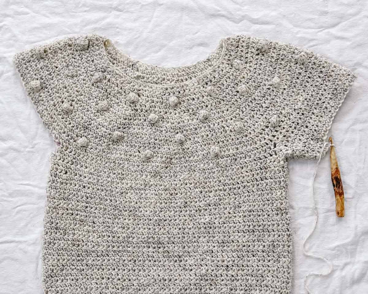 An in-progress crochet top down bobble sweater with a crochet hook.