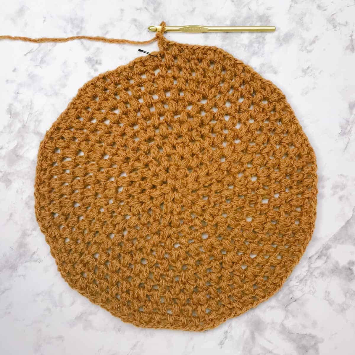 An in-progress crochet beret pattern with a hook and stitch marker.