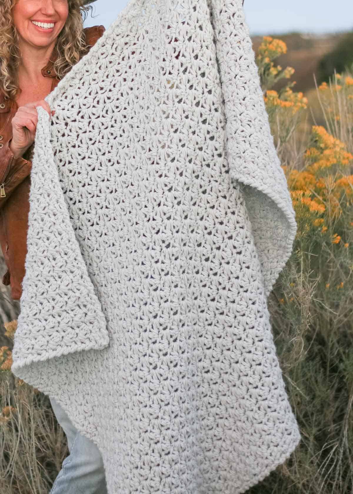 A woman smilling while holding a fast, crochet chunky blanket.