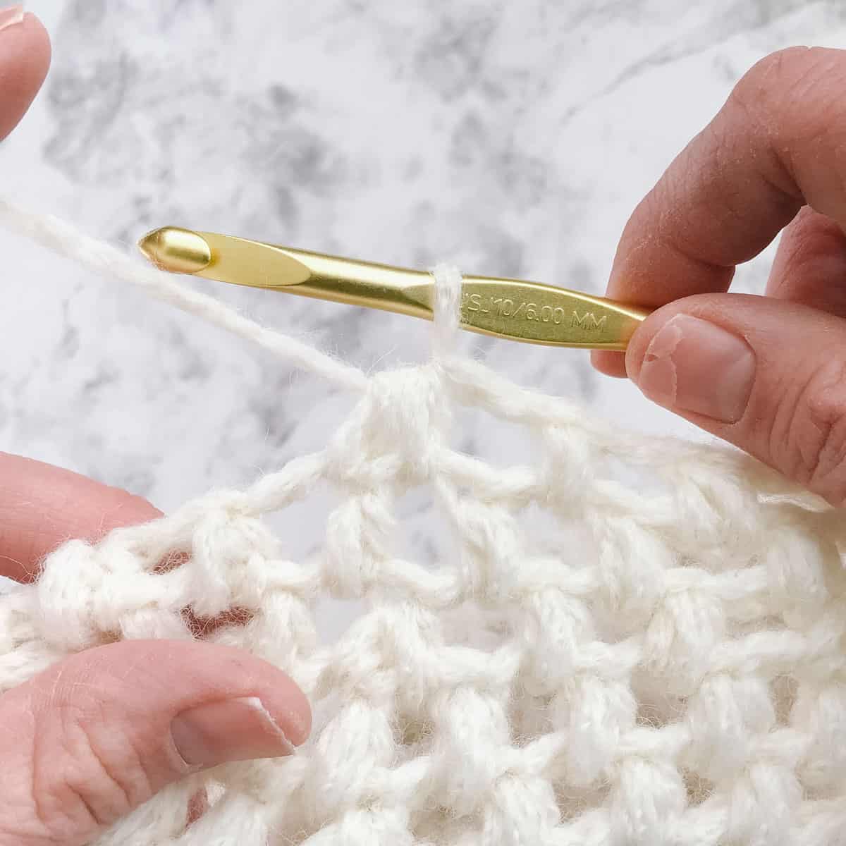 An in-progress puff stitch crochet beret tutorial and gold crochet hook.