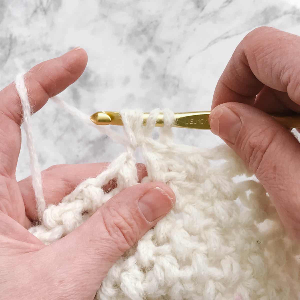 An in-progress puff stitch crochet white beret and crochet hook.