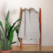 A bulky crochet throw blanket draped on a wooden ladder.