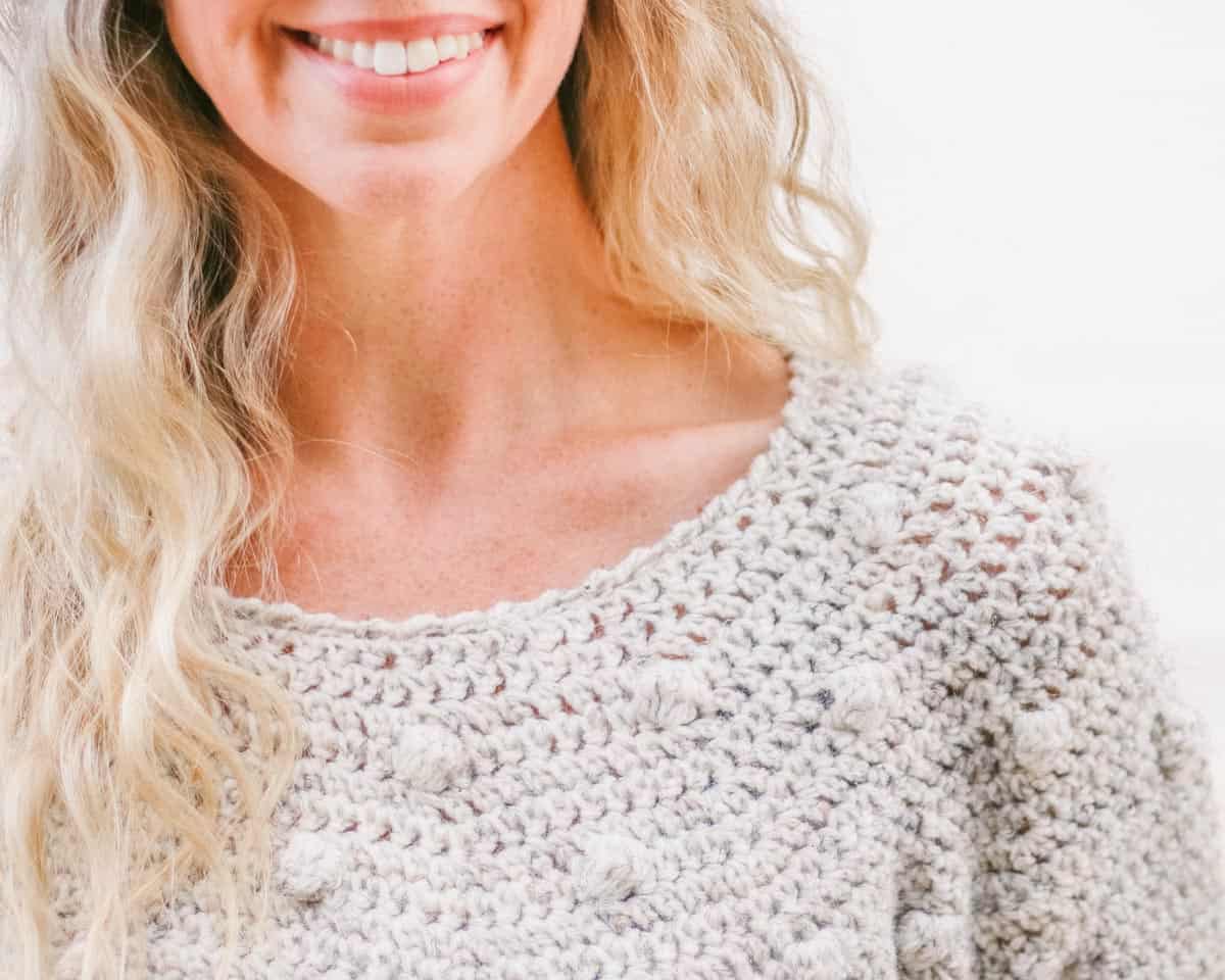 A woman smiling wearing a crew neck bobble sweater.