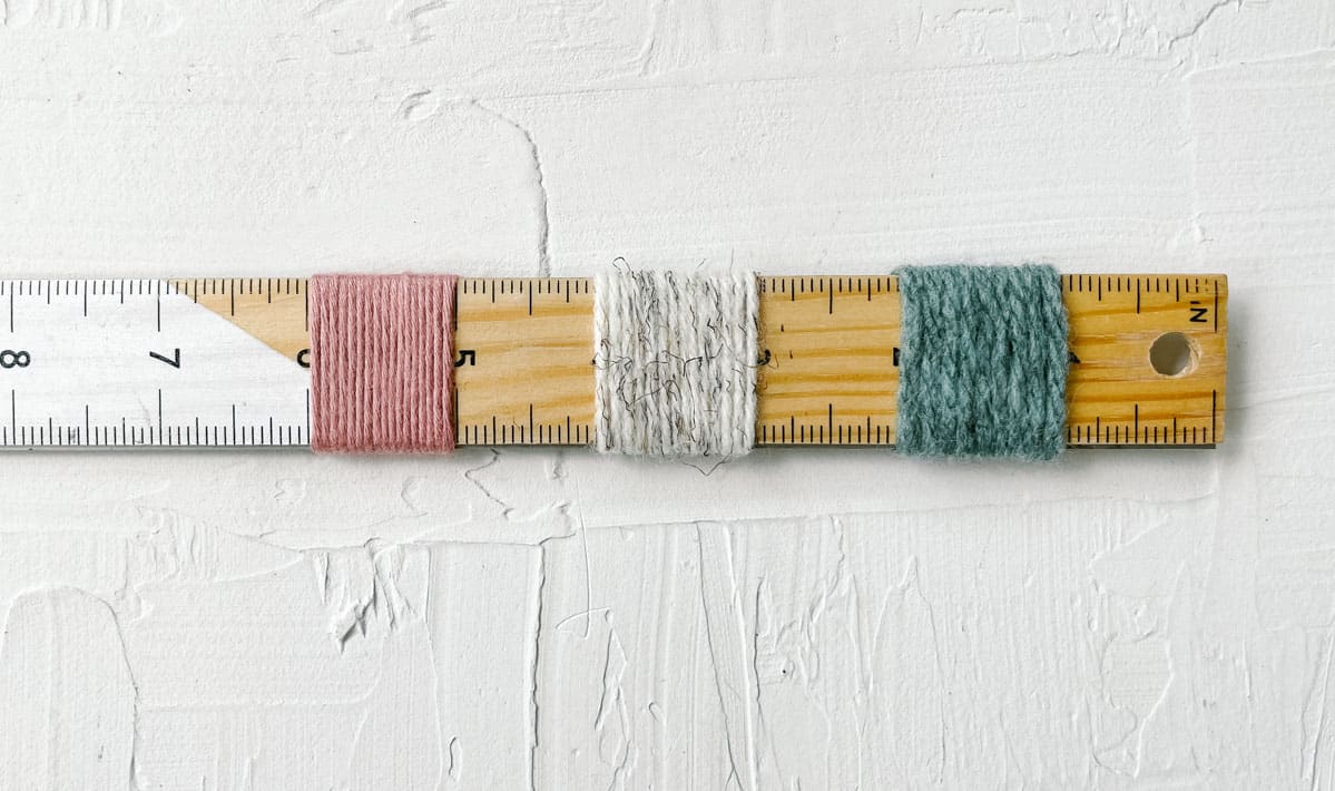 A ruler with three different yarns wrapped around it.