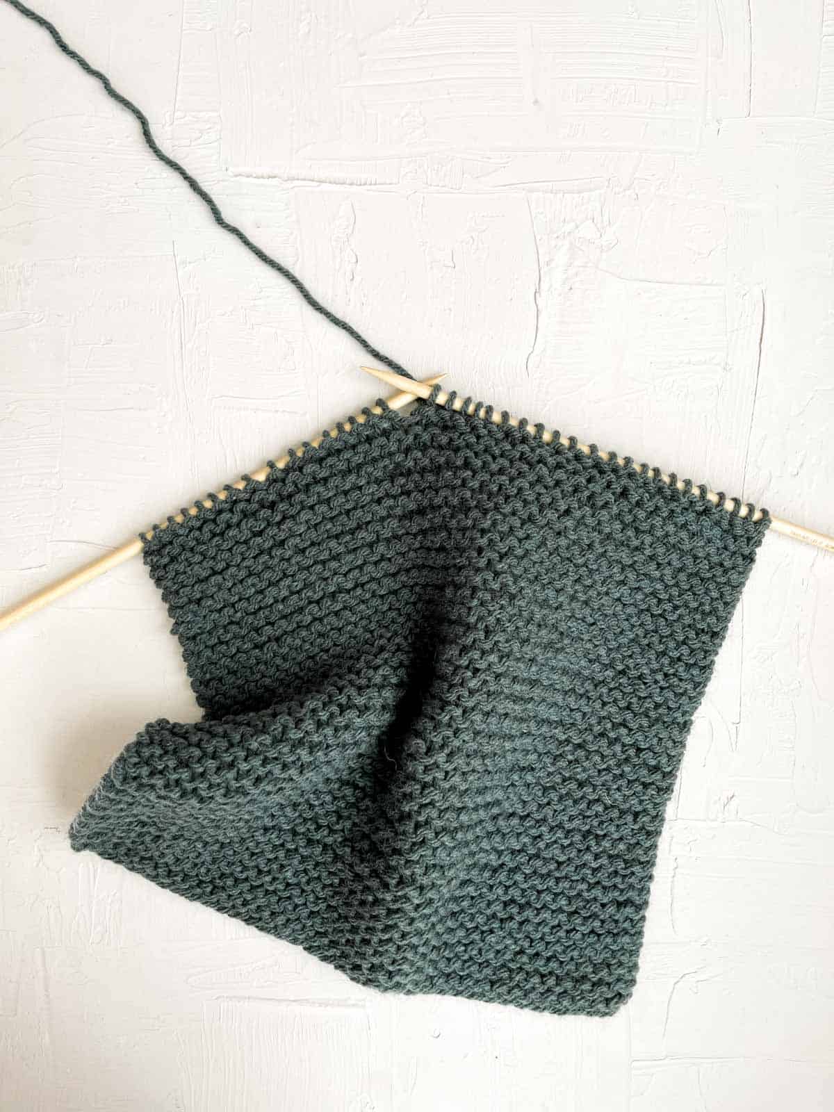 Straight knitting needles working garter stitch in chunky green yarn.