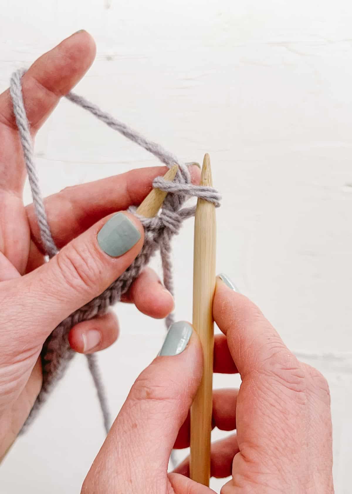 A wooden knitting needle inserted in first cast on stitch.