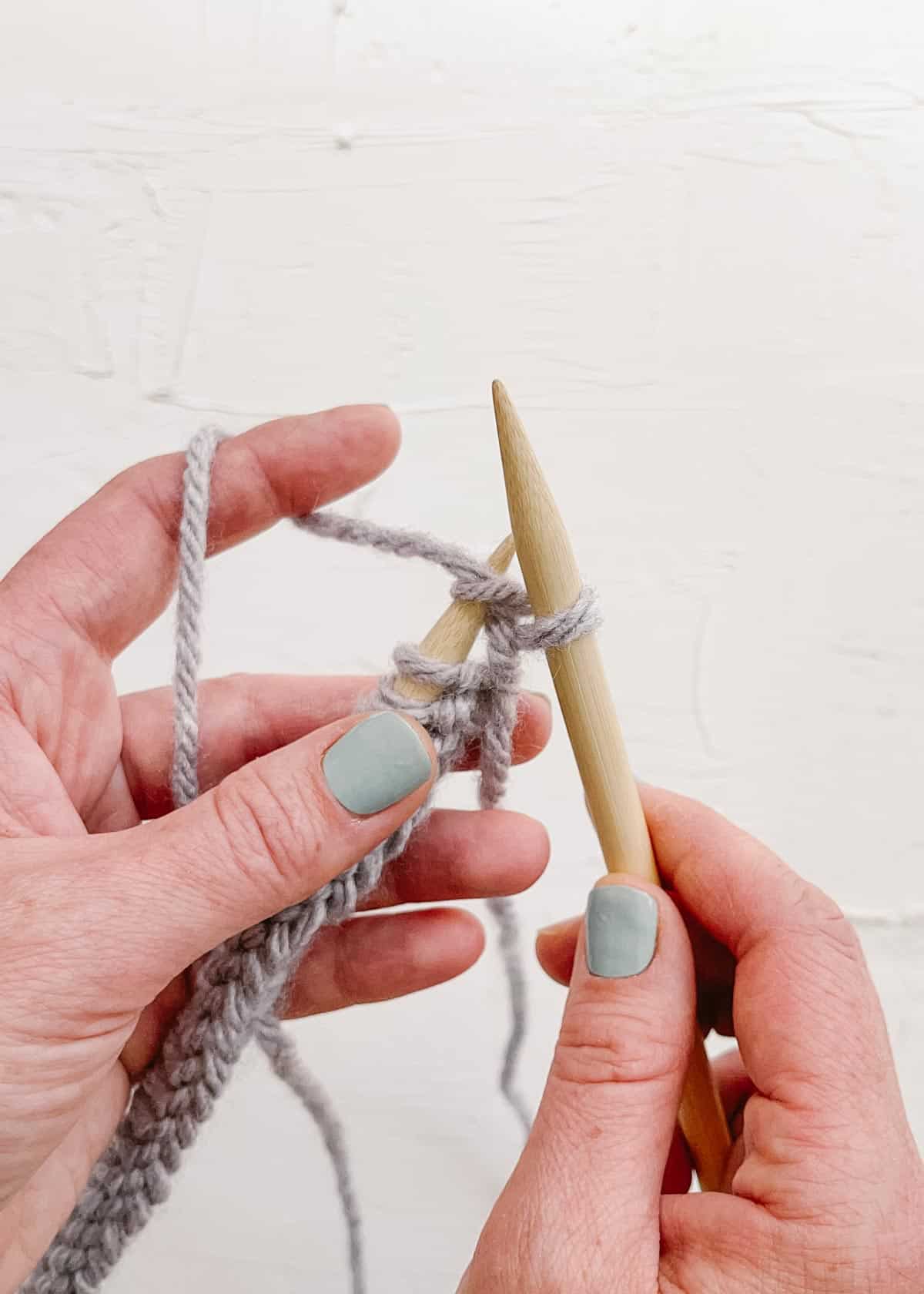 A wooden knitting needle lifting first knit stitch off opposite needle.