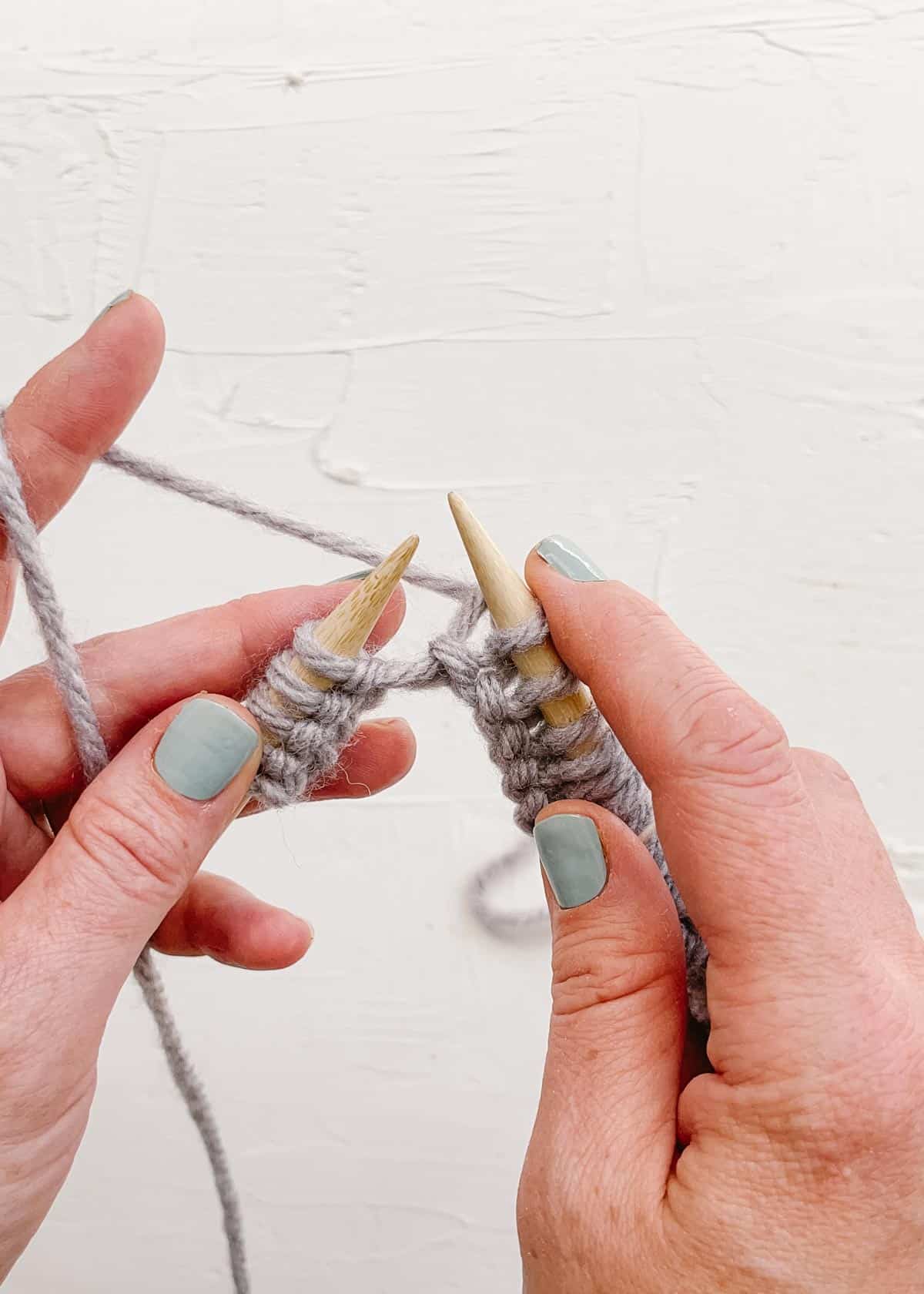 Knitting stitches with purple yarn on wooden needles.