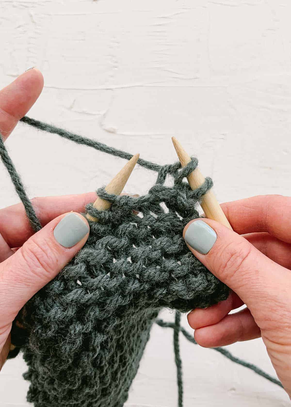 Two knit stitches complete on wood knitting needles.