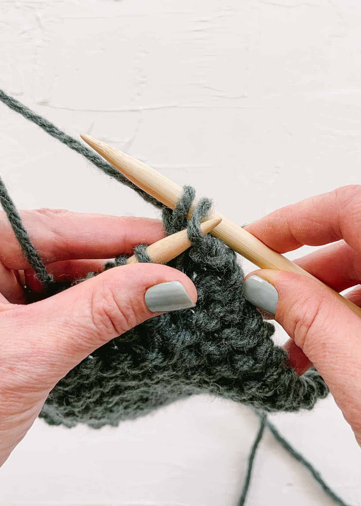 Wooden knitting needle lifting far right stitch over second stitch to cast off one.