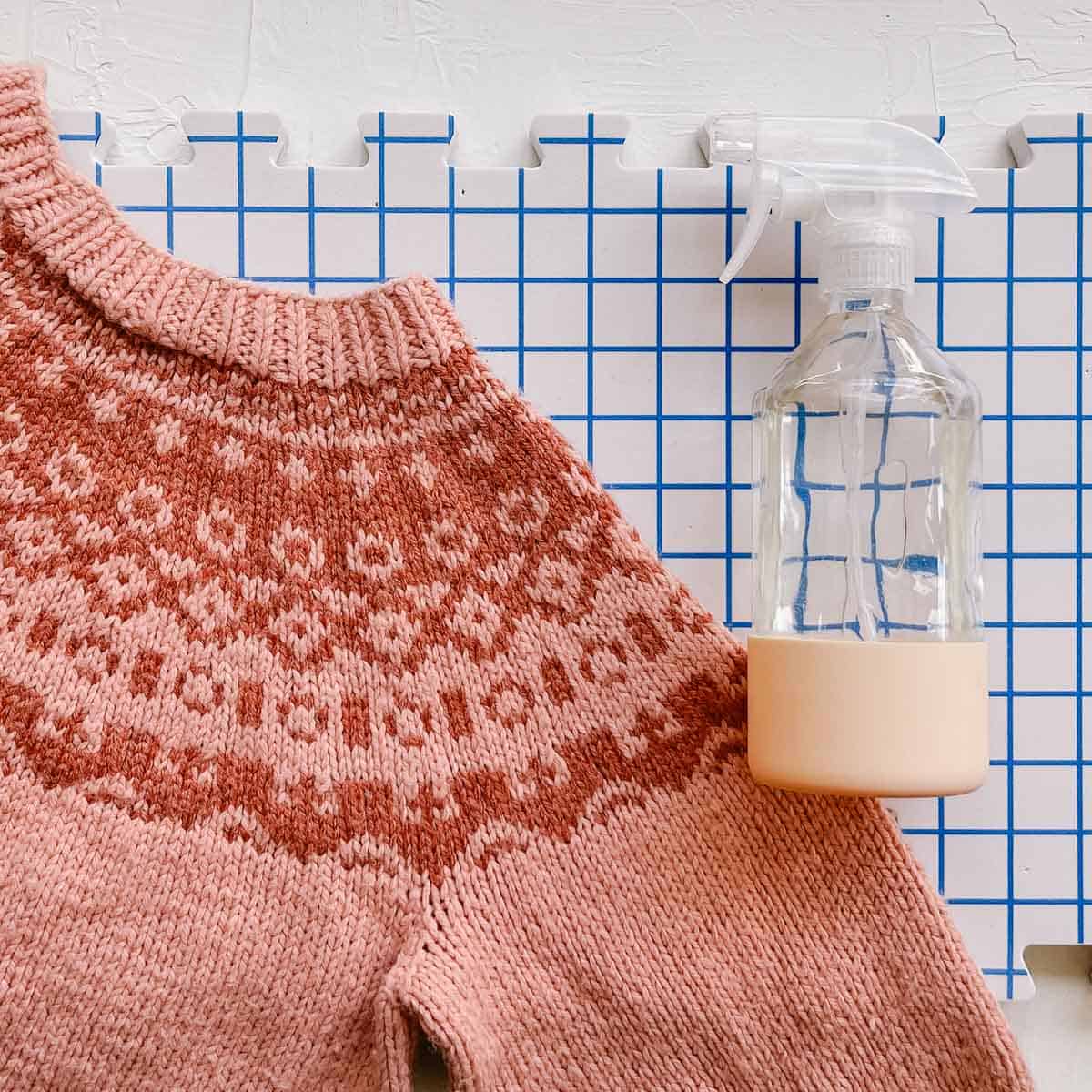 Spray bottle next to a hand knit sweater on a blocking mat.