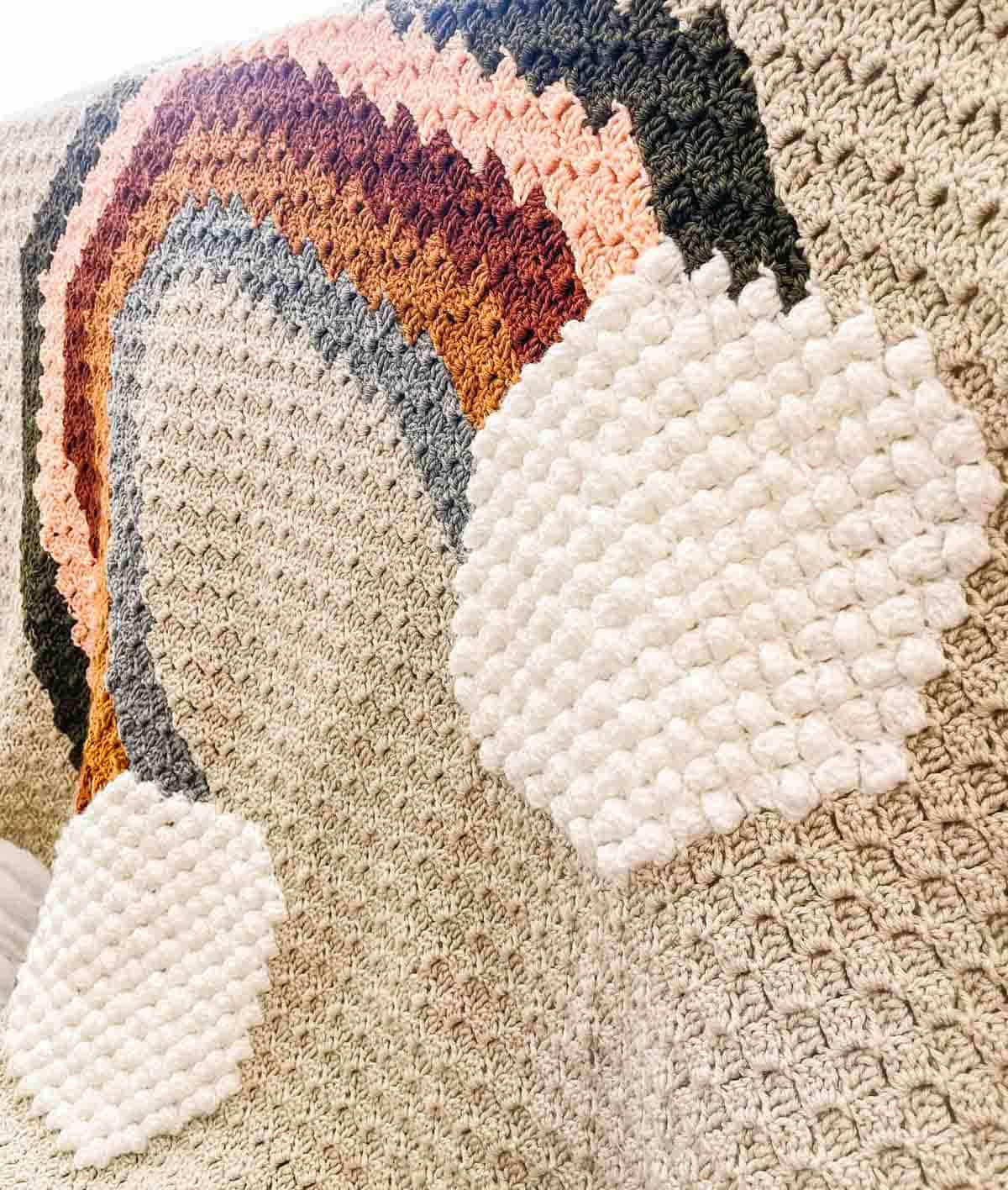 Crochet puff stitch clouds on a rainbow blanket.