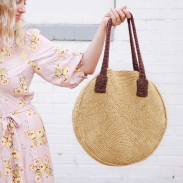 A woman holding a mustard-colored round crochet bag.