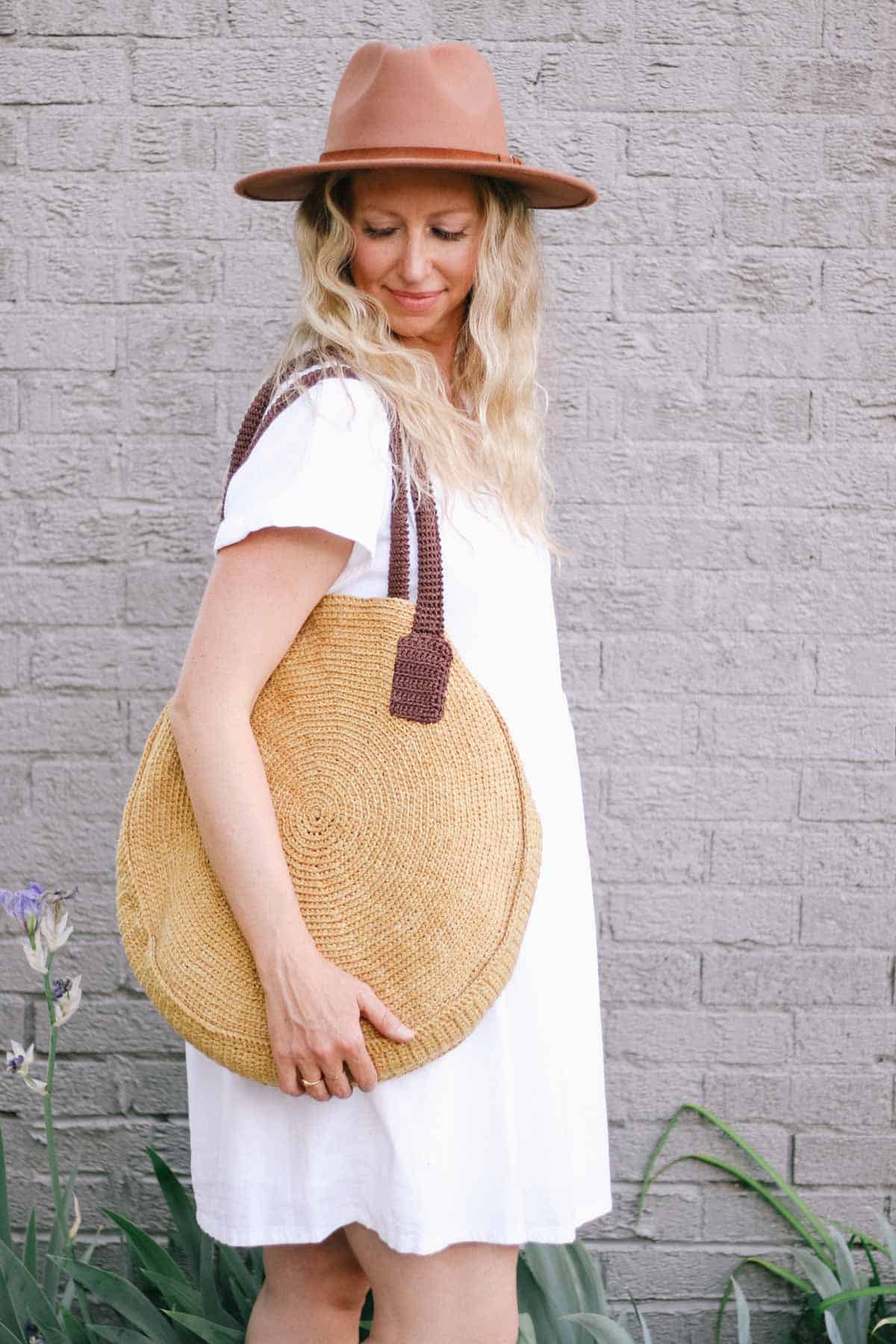 Woman holding a large round crochet bag over her shoulder.