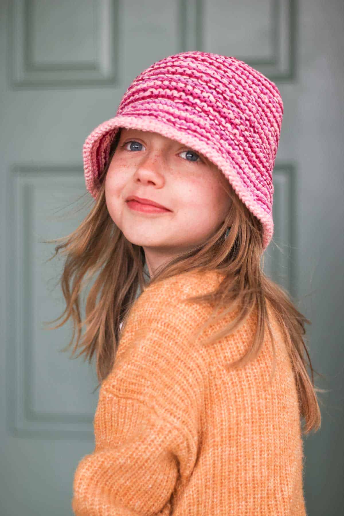 Child wearing a pink knit bucket hat, looking in the distance.