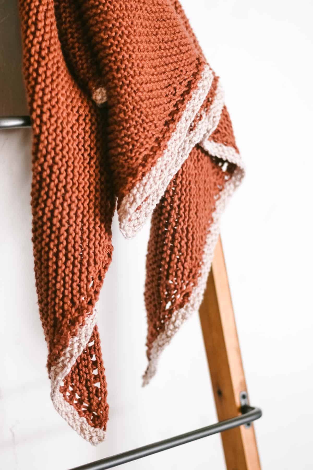Rust colored garter stitch knit triangle scarf draped over a blanket ladder.