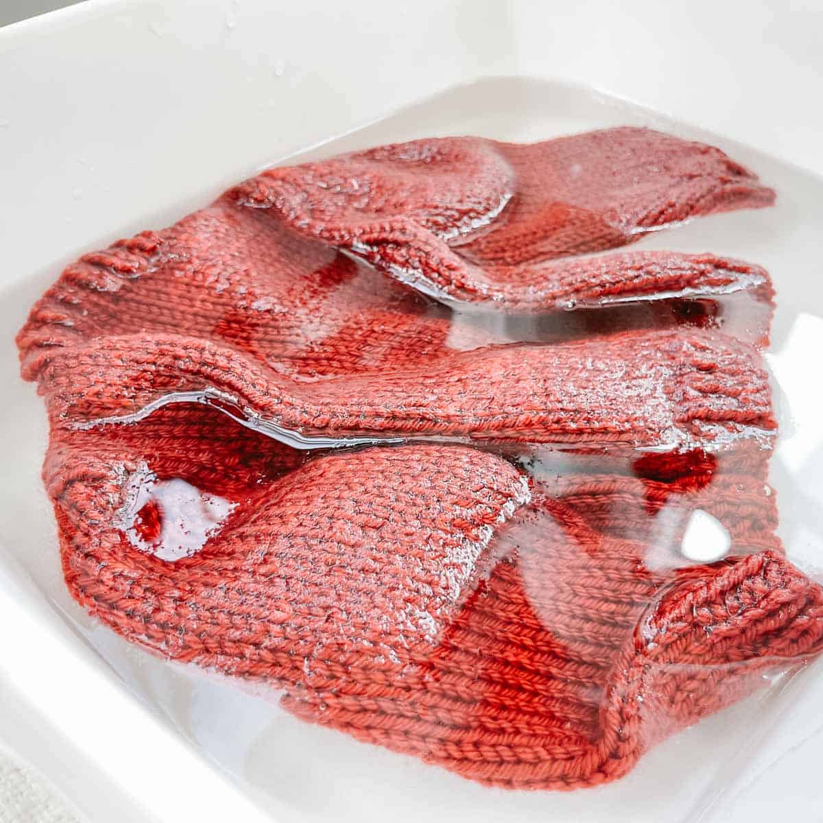 A red knit sweater soaking in a basin of water.