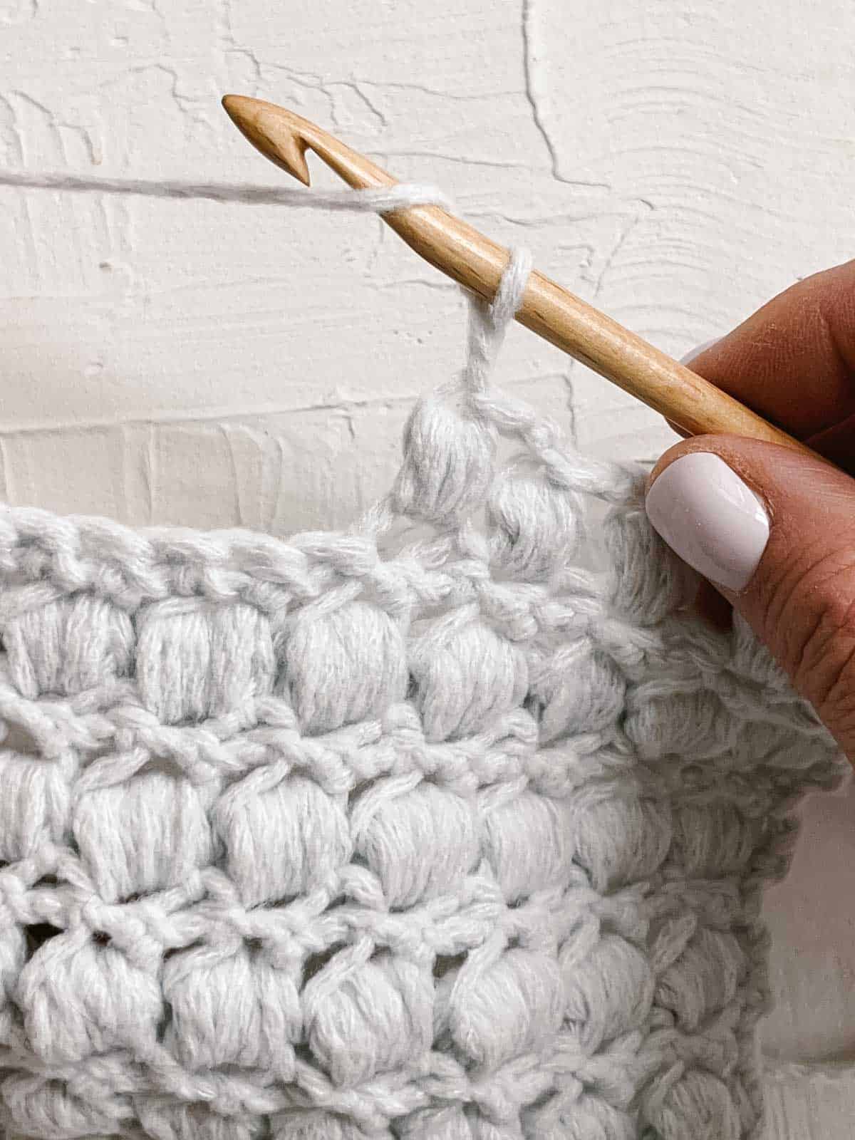 Yarn over with a wooden crochet hook in a swatch of puff stitches.