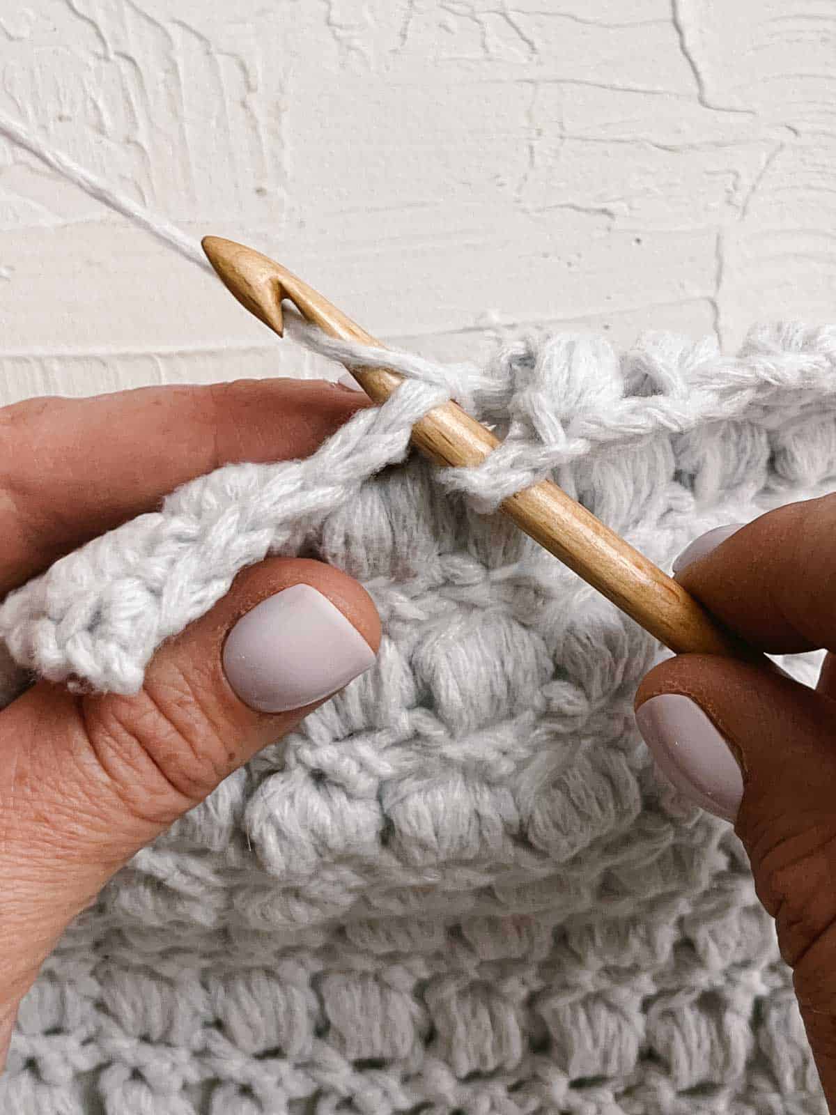 Bamboo crochet hook pulling grey yarn through a stitch.