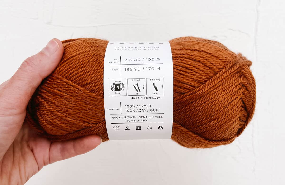 A hand holding a brown colored yarn skein.
