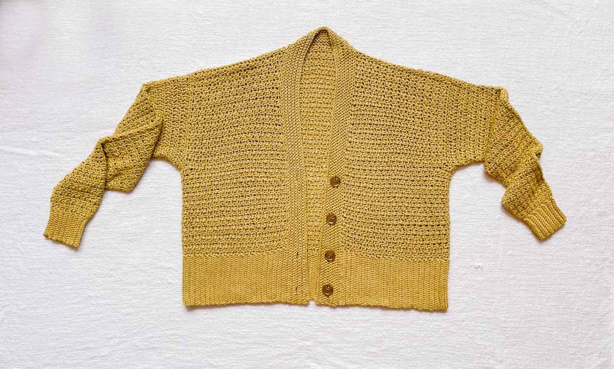 A mustard-colored crochet cropped cardigan laying flat.