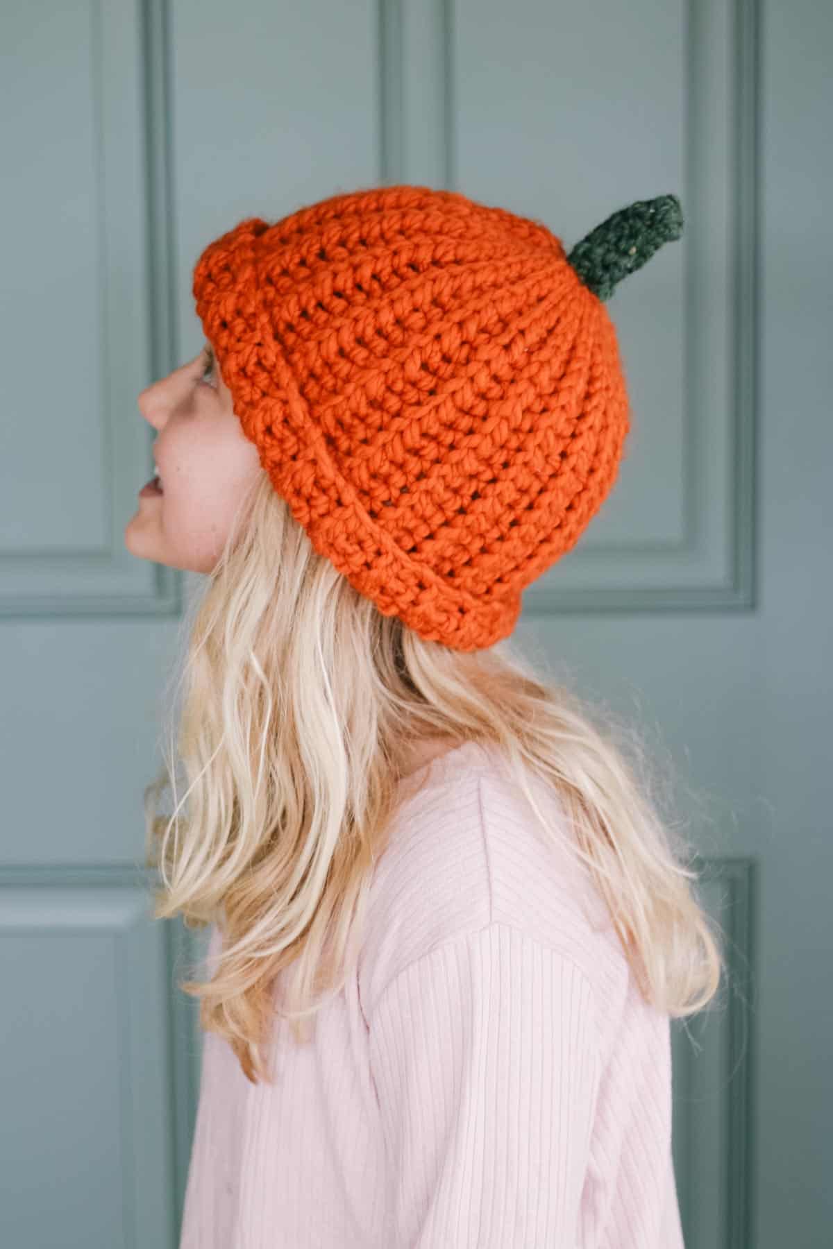 A girl wearing an orange pumpkin crochet beanie.