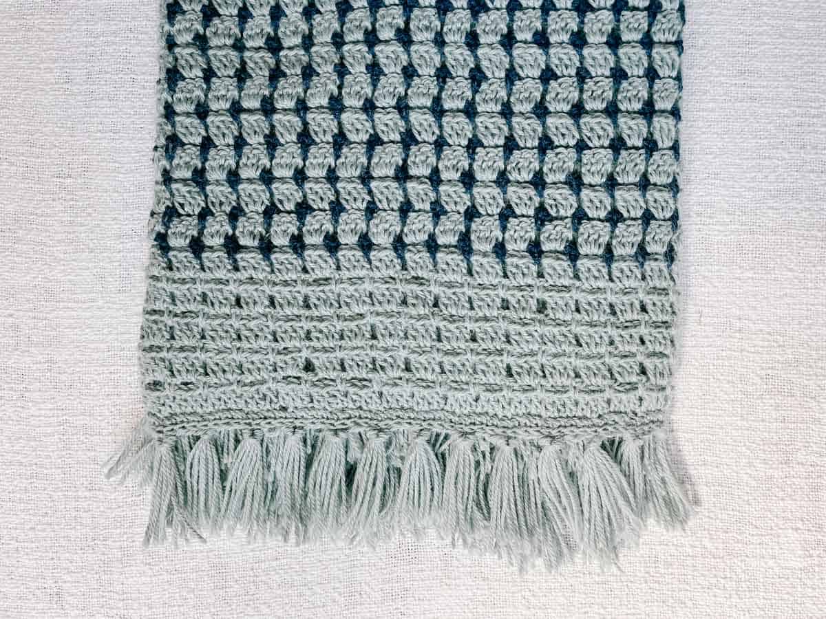 Fringe along the edge of a blue striped double crochet blanket.