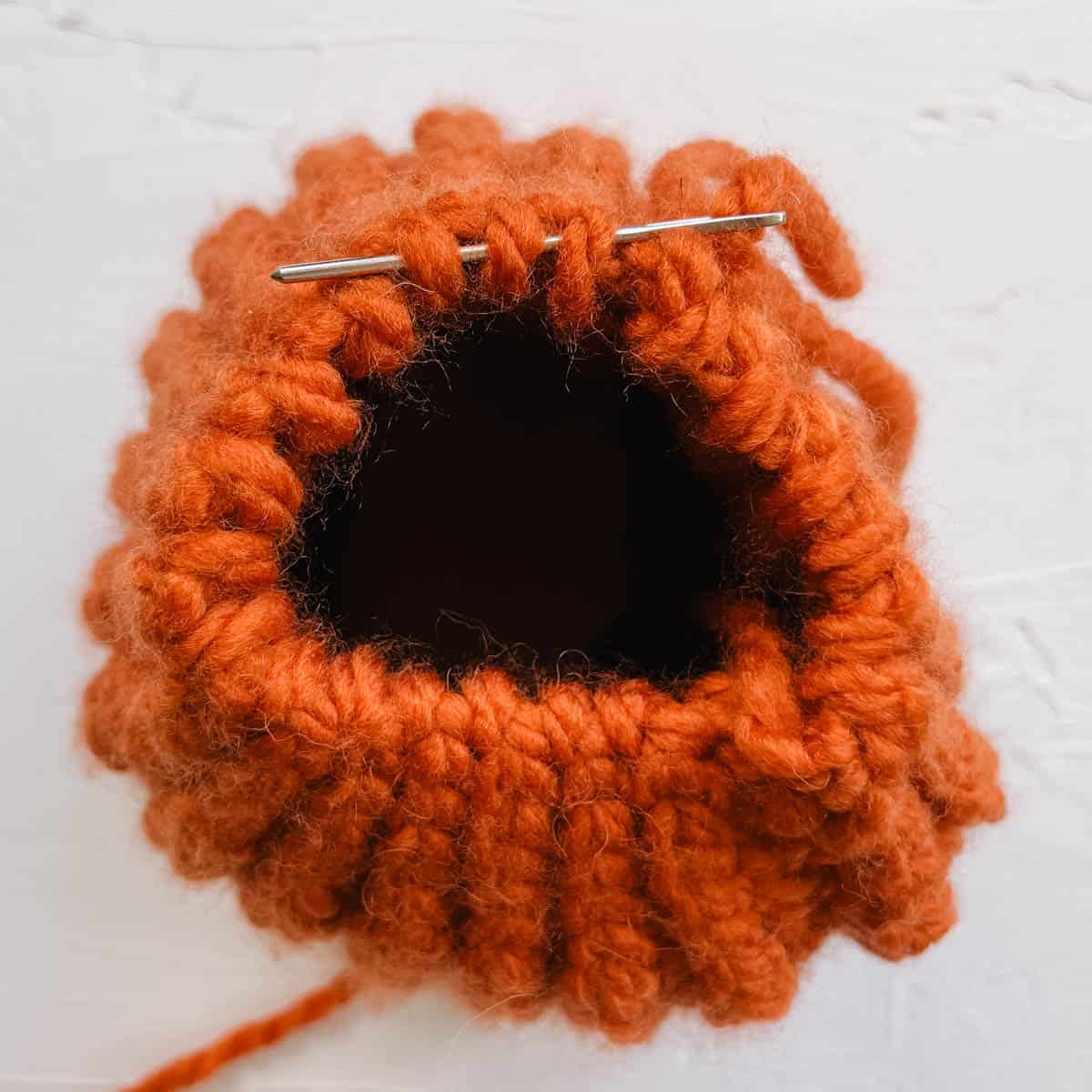 Top view of a crochet tube being closed into a pumpkin hat.