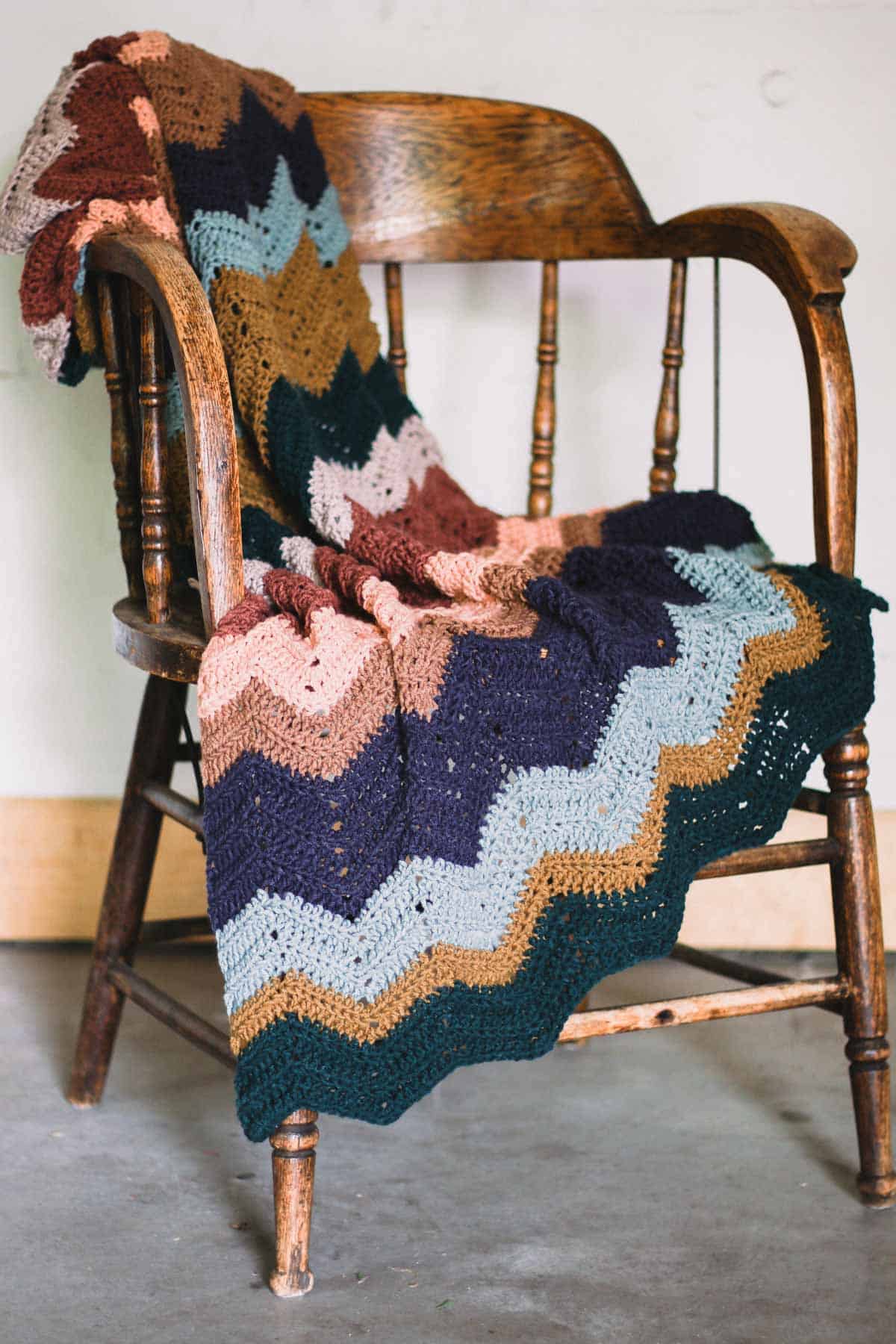 A crochet chevron blanket with zig zag stripes draped over a rustic wood chair.