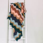 A chevron crochet blanket tossed casually over a white ladder.