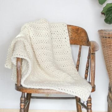 A basic crochet blanket draped over a wooden chair.