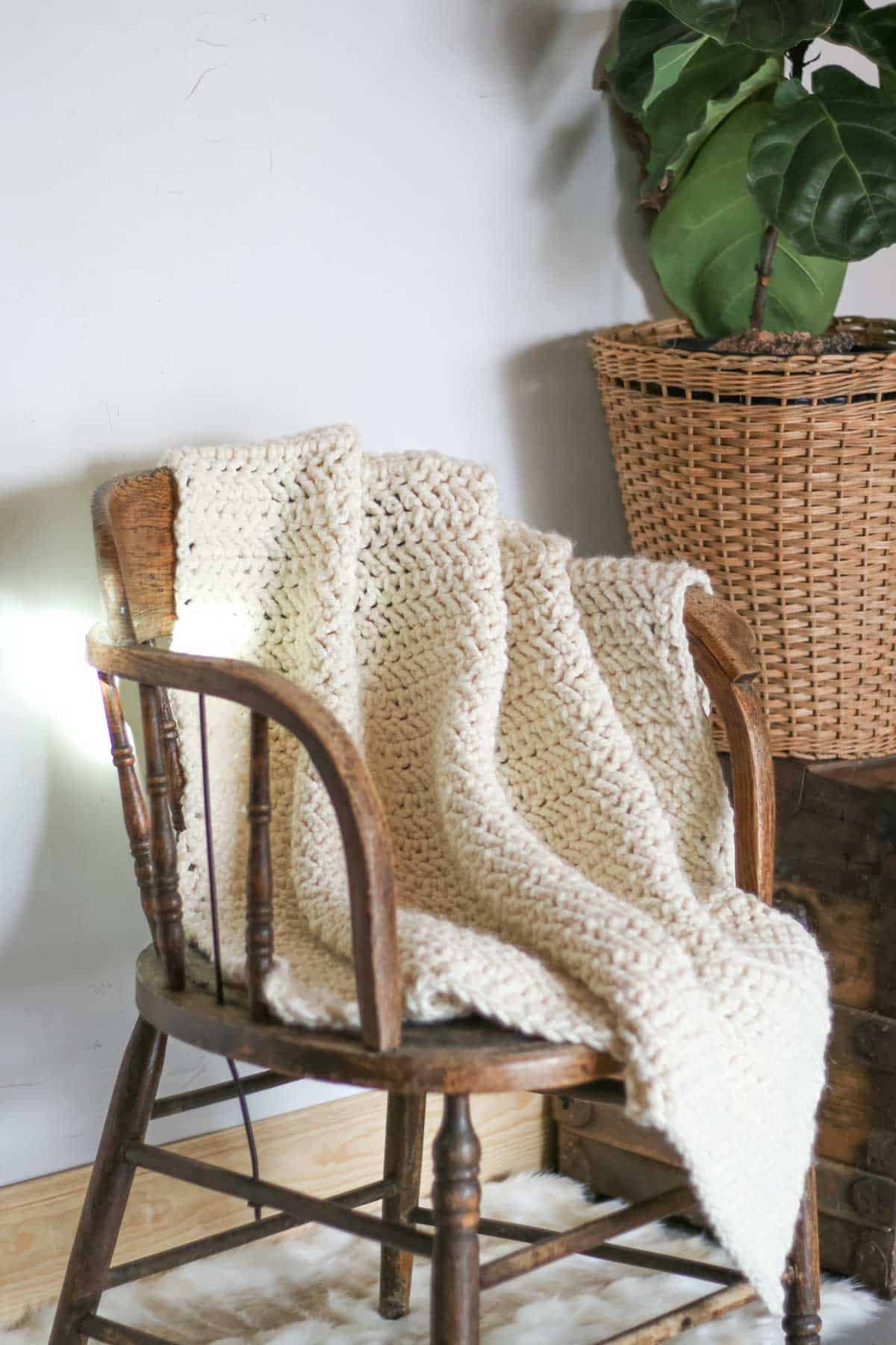 A simple crochet blanket draped over a wooden chair.