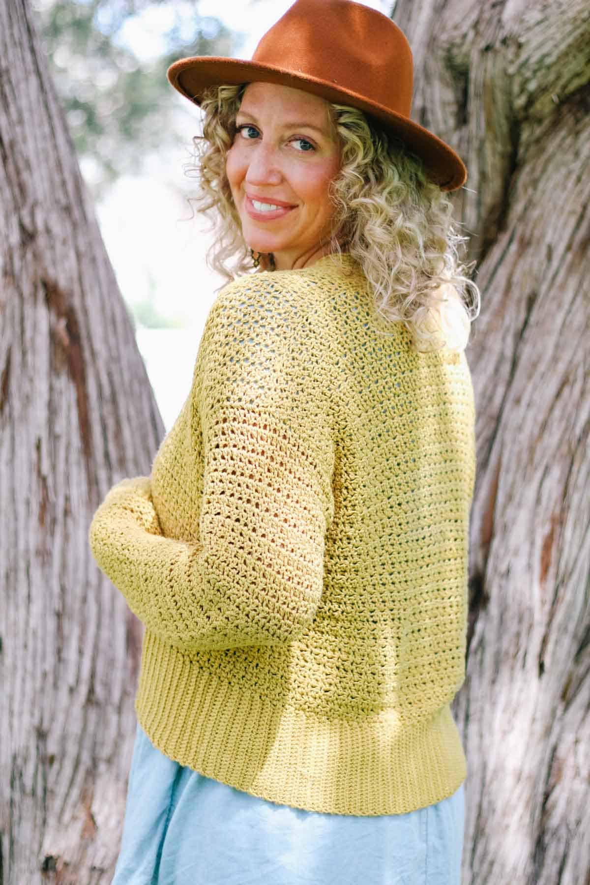 A woman wearing a cropped crochet sweater smiling over her shoulder.